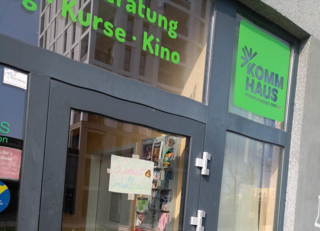 Eingangstür zum KOMM-Haus mit einem selbstgebastelten Schild auf dem Linux Installationscafé steht.
